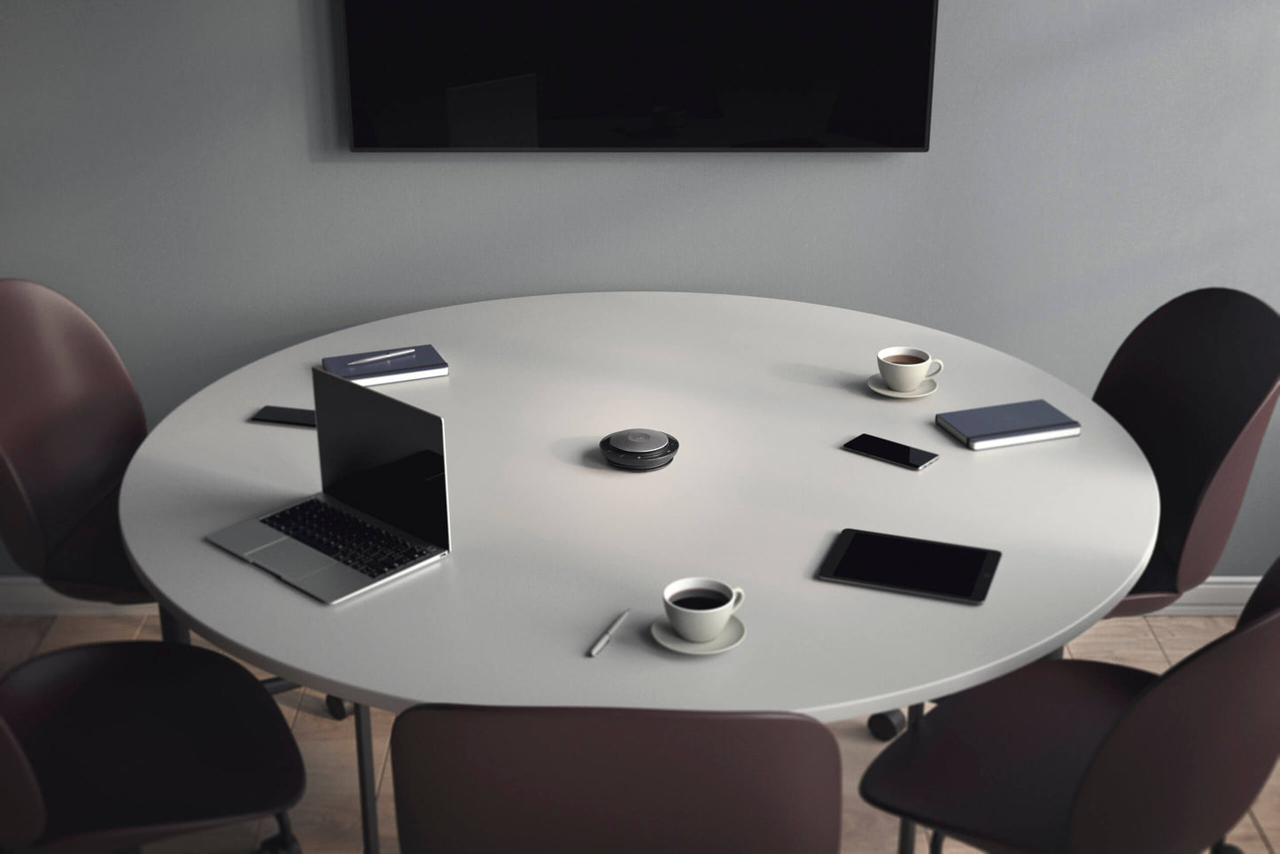 Round table with laptop and three smart phones around the table, cops of coffee and notebooks by the smartphones and a JabraSpeak 750 in the centre of the table