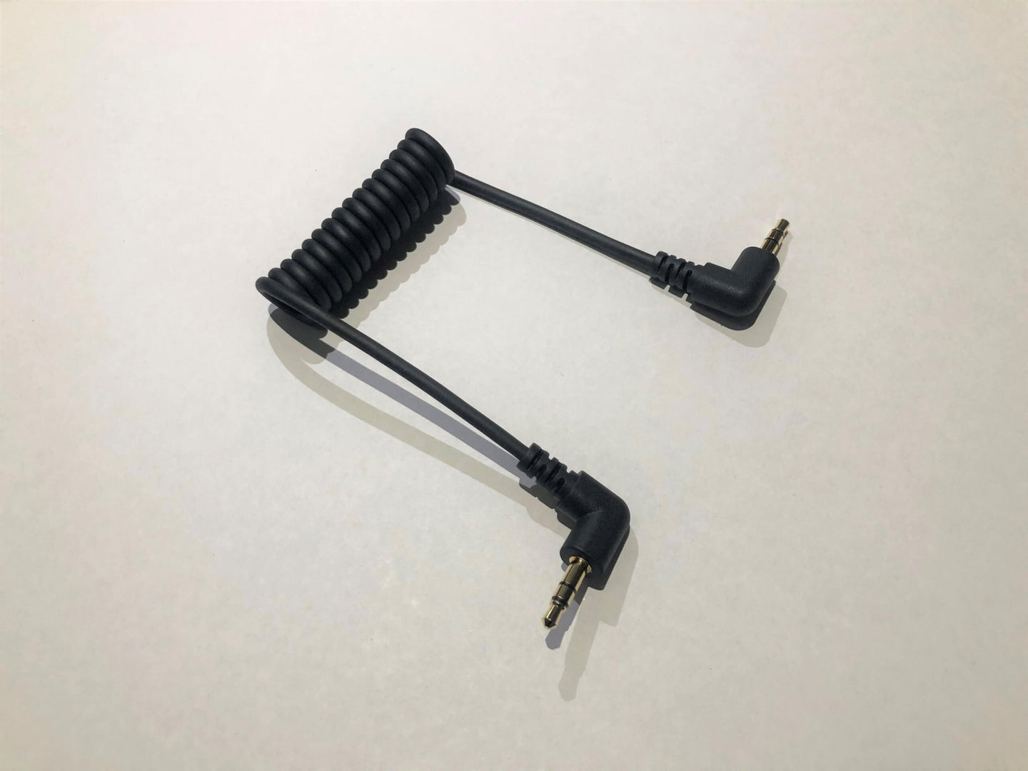 A black coiled audio cable with 3.5mm L-shaped plugs at both ends, intended for connecting an audio recorder to a digital camera.