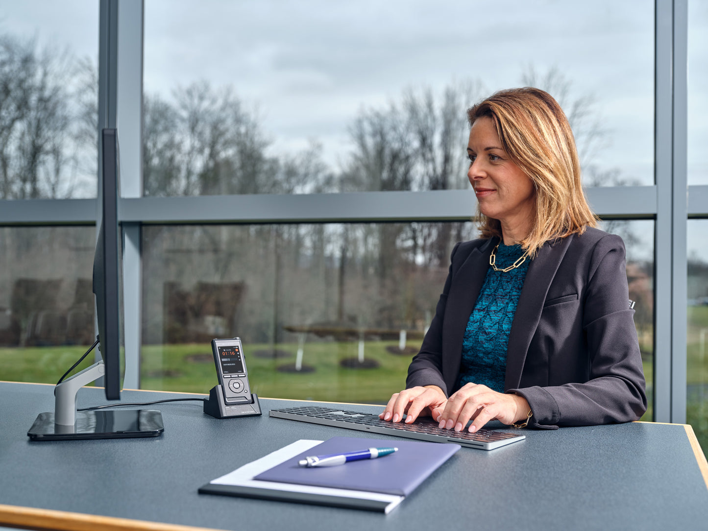 Woman sitting at a desk, using OM System DS-9100 dictaphone for hands free dictation