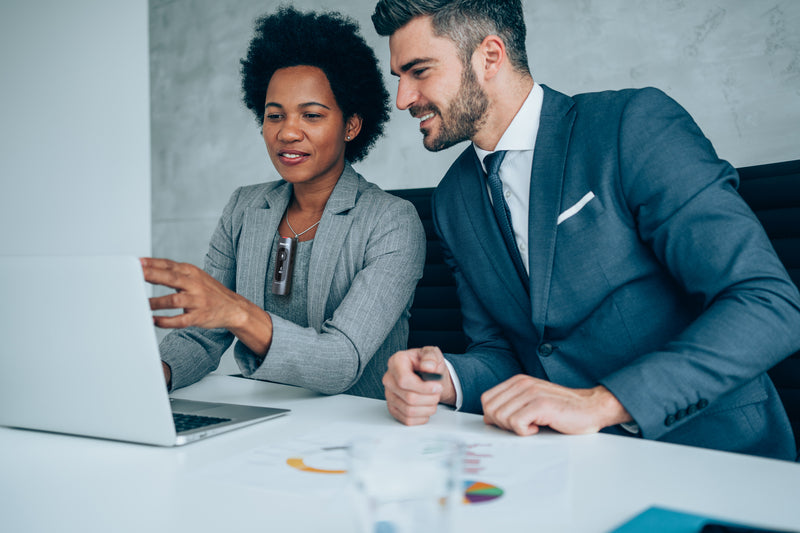 To professionals in front of a computer with one wearing the Philips SpeechMike Ambient Wearable AI Assistant to capture their conversation.