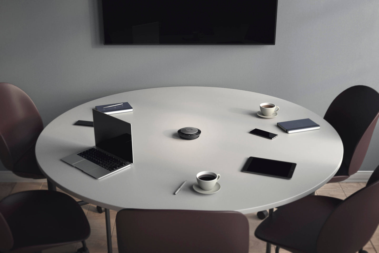 Round table with laptop and three smart phones around the table, cops of coffee and notebooks by the smartphones and a JabraSpeak 750 in the  centre of the table