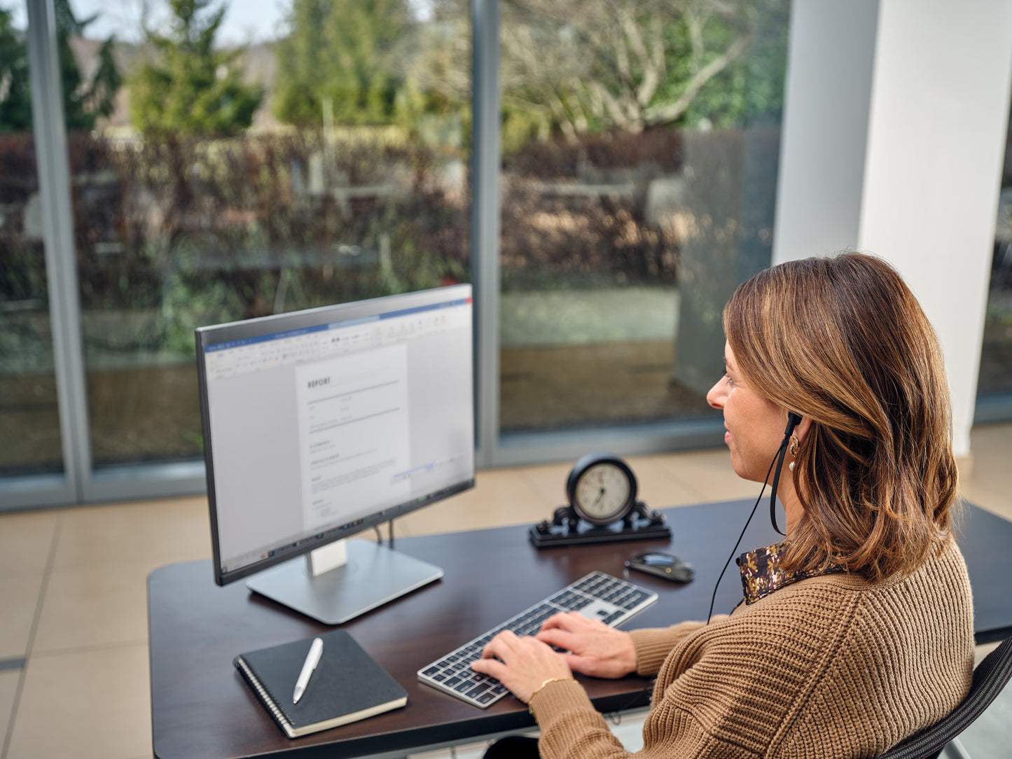 Woman sitting at a computer, using headset and foot pedal to transcribe audio