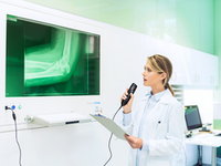 Woman in lab coat sitting at desk with X Ray on computer screen and dictating into Philips SpeechMike