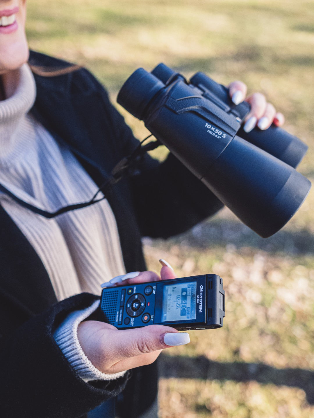 OM System WS-883 digital voice recorder being used in the field by a person with binoculars
