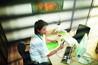 Woman sitting at cluttered desk, dictating into Philips SpeechMike LFH3200, which is tethered to computer