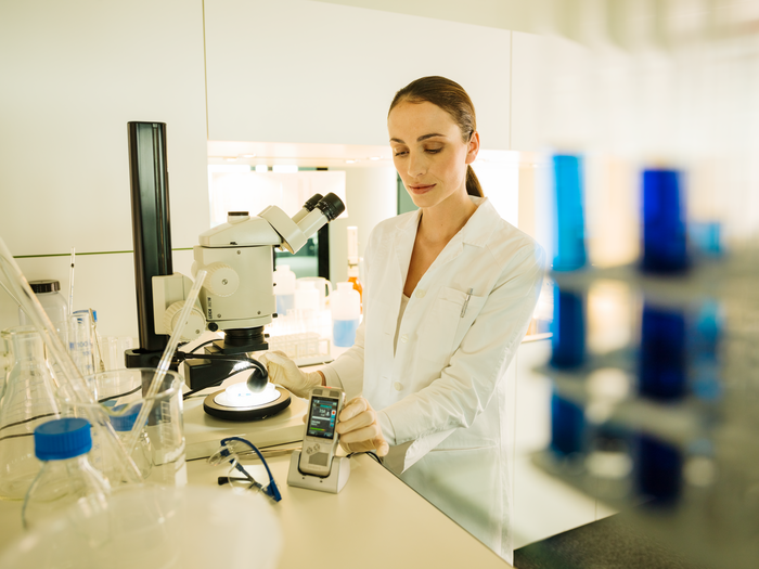Woman in laboratory setting, with microscope, using Philips DPM8000 in docking station for hands free dictation.
