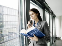 Woman standing by a window, holding a reference book and dictating into OM System DS-9100 dictaphone